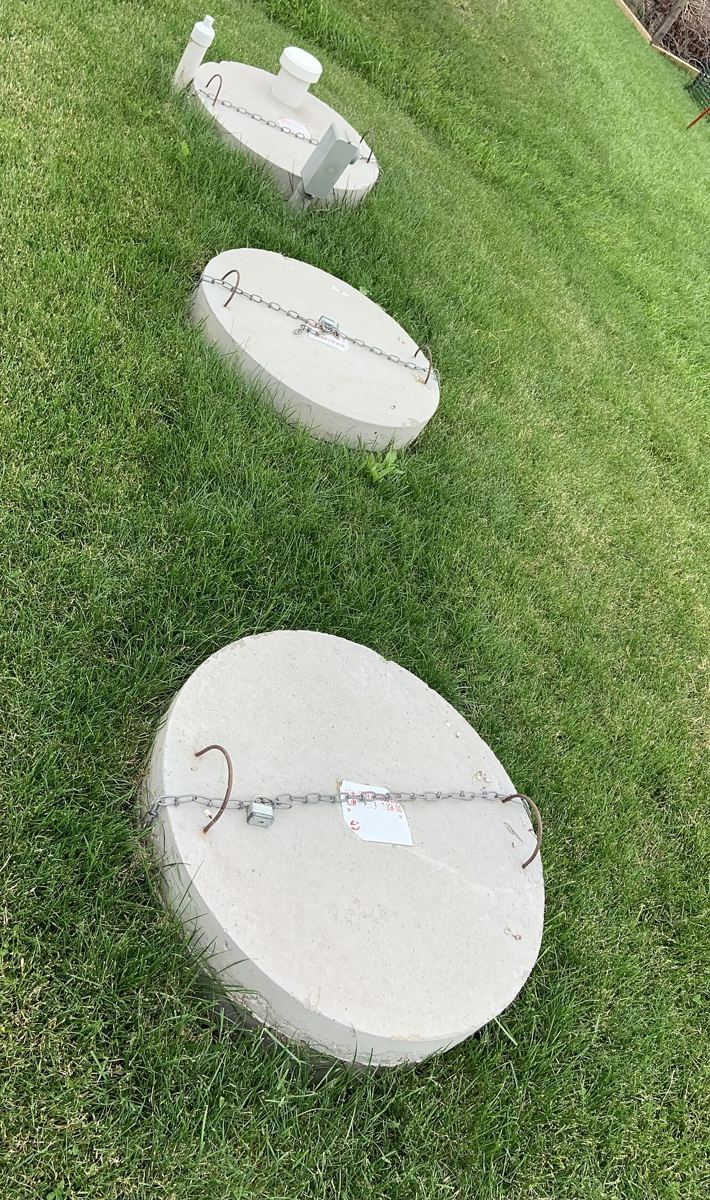 Three round concrete septic tank access lids with lifting chains in a mown lawn