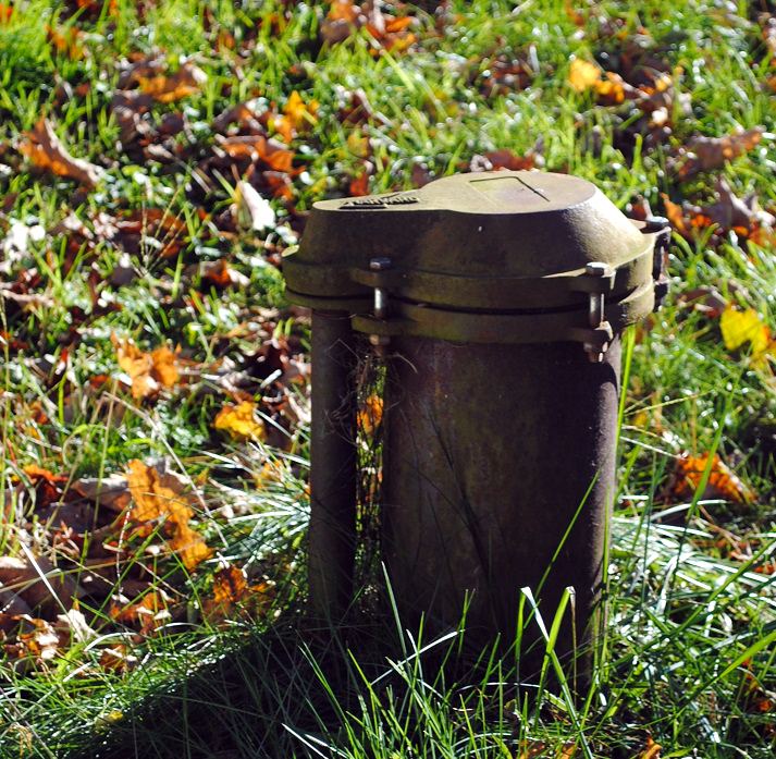 Steel well casing with a vented well cap in a lawn covered with autumn leaves